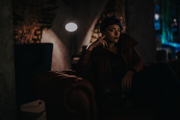 A woman sits thoughtfully on a classic leather sofa in a dimly lit vintage room, evoking moodiness...