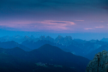 Sunset in the mountains. Red and orange burning sky horizon behind the alpine mountain range. Rocky mountain peaks of the Dolomites at sunset and dawn at sunrise light sunrays going through the clouds