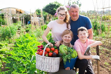 Obraz premium Parents with children posing with a basket of ripe vegetables in the garden