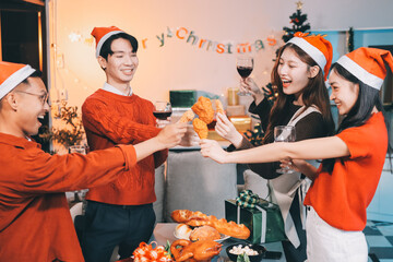 Group of young Asian man and women as friends having fun at a New Year's celebration, holding gift boxes standing by Christmas tree decoration, midnight countdown Party at home with holiday season.