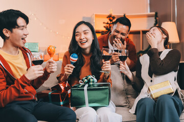 Group of young Asian man and women as friends having fun at a New Year's celebration, holding gift boxes standing by Christmas tree decoration, midnight countdown Party at home with holiday season.