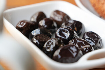 A plate filled with Delicious Black Olives is presented beautifully in a White Serving Dish