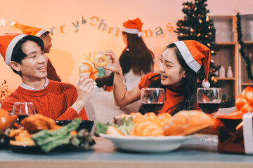 Group of young Asian man and women as friends having fun at a New Year's celebration, holding gift boxes standing by Christmas tree decoration, midnight countdown Party at home with holiday season.