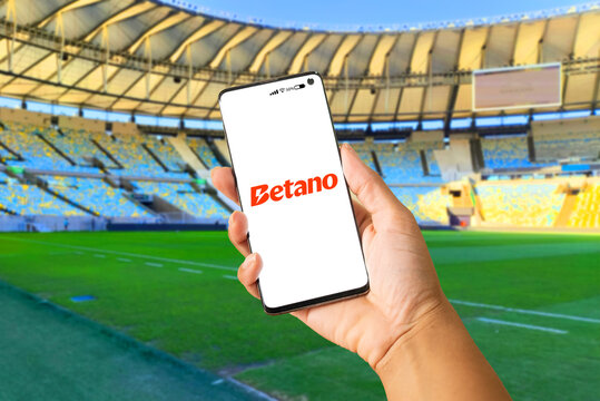 Hand holding a smartphone with the Betano betting provider app on the screen. Background with a football stadium. Rio de Janeiro, RJ, Brazil. November