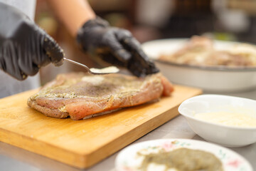 Chef spreading seasoning on raw meat with a spoon in a professional kitchen