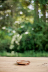 Vertical photo and selective focus. Wood grain end table with round wood base on blur green forest background for montage product display or design