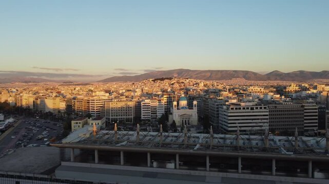 Vis&atilde;o a&eacute;rea do centro urbano de Atenas ao fim do dia, com o sol se pondo atr&aacute;s de seus edif&iacute;cios hist&oacute;ricos, criando uma atmosfera &uacute;nica da cidade grega