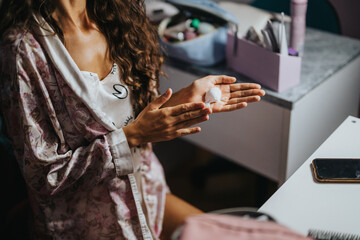 A woman applying moisturizer to her hands as part of a morning beauty routine. She is wearing a...