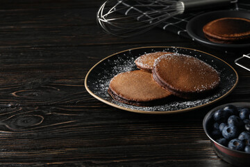 Chocolate pancakes on plates and bowl with berries on wooden background, space for text