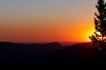A breathtaking sunrise over mountains with vibrant orange hues and silhouette of tree during a clear morning sky