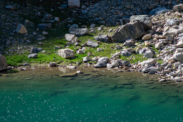 Tranquil mountain turquoise lake with surrounded by rocky terrain and vibrant greenery during a sunny day in high-altitude landscape