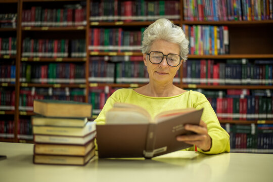 Elder woman sitting enjoys reading book in quiet of the library appears focused and content books with the idea of self-growth and discovery at any stage of life.