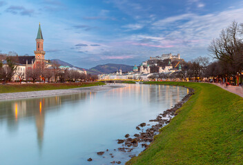 A serene view of the Salzach River in Salzburg, Austria, with reflections of St. Andrew's Church and the Hohensalzburg Fortress in the water