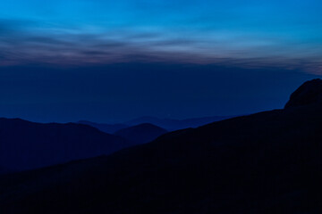 A peaceful twilight view from a mountain summit showcasing distant peaks and a fading sunset in the tranquil evening sky