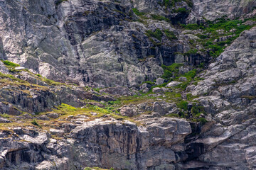 Rocky mountain landscape with lush greenery and rugged terrain under bright daylight in a natural outdoor setting