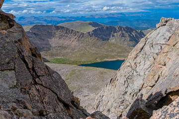 A breathtaking view from a Mount Blue Sky (Mount Evans) in the wilderness, showcasing a serene lake surrounded by rugged terrain and distant mountains under a clear blue sky