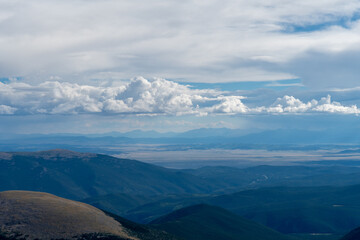 Expansive view from the summit of a mountain in Colorado during late afternoon under a partly cloudy sky showcasing rolling hills and distant peaks