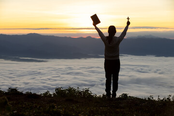 Silhouette of a woman praying on a mountain at sunrise. Young woman praying to God.