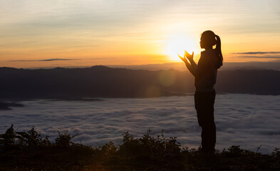 Fototapeta premium Silhouette of a woman praying on a mountain at sunrise. Young woman praying to God.