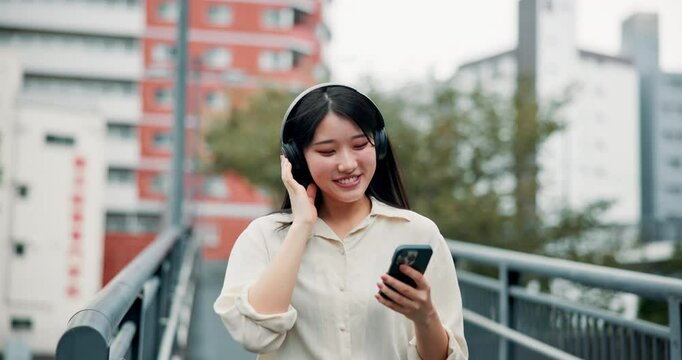 Japanese woman, headphones and mobile phone for music, listening and entertainment in city for podcast. Female person, technology and happiness for audio, radio or streaming on app or online playlist