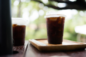 Iced americano in transparent plastic glass on the table in the garden nature background and bokeh light