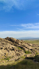 Landscape with bizarre mountains, rocks with hollows against a blue sky, hills, vegetation and a city in the background