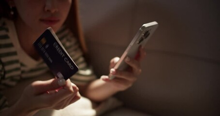 A young woman smiles while shopping online holding her credit card and phone reflecting the joy of digital spending.