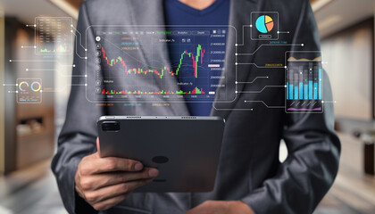 Business professional analyzing stock market trends on a tablet with digital charts and graphs displayed in a modern office environment