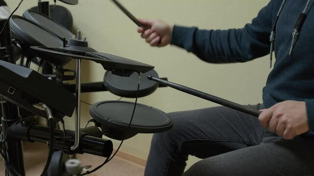 Male musician is skillfully playing electronic drum kit with drumsticks, creating rhythmic patterns and beats in music studio, demonstrating his passion for drumming and music creation