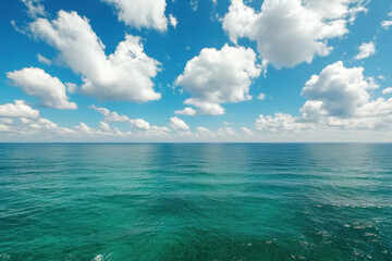 Obraz premium A serene seascape featuring calm turquoise waters under a bright blue sky filled with fluffy white clouds, evoking tranquility and natural beauty.
