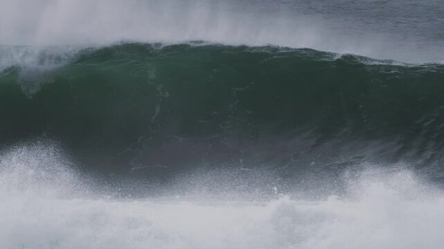 Rolling wave curls into a barrel, mist blowing off in dramatic, stormy blue light
