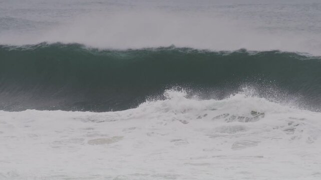Massive wave crashes into a barrel, with mist blowing off the crest at blue hour sunset