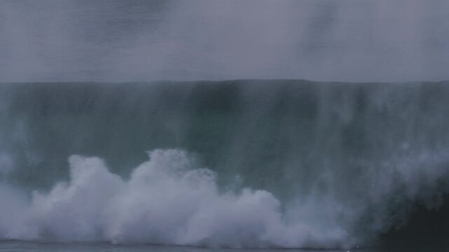 Massive wave rolls into a barrel, mist blowing off the top in stormy blue conditions