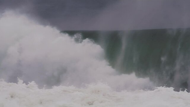 Rolling wave curls into a massive barrel, mist blowing off in dark, moody blue light