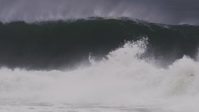 Slow motion shot of a powerful barrel wave, mist drifting off the peak under stormy skies