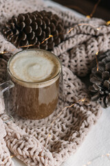 New Year, Christmas card. Coffee with milk in a glass mug among the cones on the blanket. Vertical photo