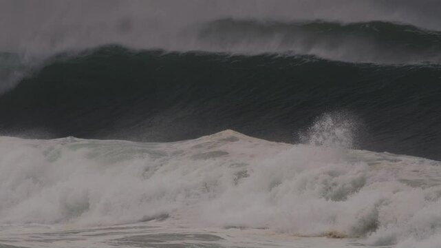 Large wave crashes, forming a deep barrel with mist blowing off in moody blue light