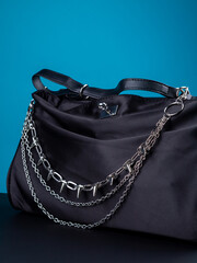 Close up of black trendy bag with silver chain on blue background