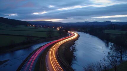 Obraz premium A peaceful evening scene with the calm waters of a river contrasted by the vibrant light trails of cars on the road.