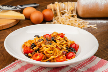 Homemade Arabiata pasta. Handmade pasta served in a white pasta dish garnished with olives and tomatoes on a dark table.
