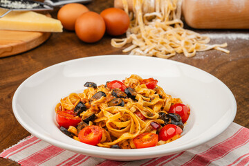 Homemade Arabiata pasta. Handmade pasta served in a white pasta dish garnished with olives and tomatoes on a dark table.