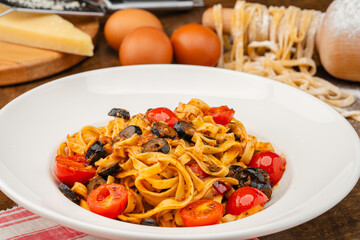 Homemade Arabiata pasta. Handmade pasta served in a white pasta dish garnished with olives and tomatoes on a dark table.