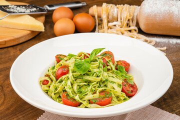 Italian Pasta with Pesto Sauce. Handmade pasta served in a white pasta plate, garnished with basil and tomatoes and served to the table.