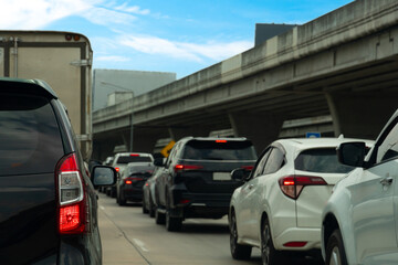 Rear side view of black car driving on the road. with other cars. Background blurred of bridge under blue sky . Cars lined up on the road in urgent traffic condition. 