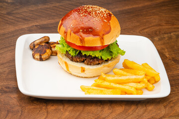 Delicious hamburger with homemade beef, tomato and lettuce. Served on a plate with French fries and mushrooms.