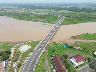 Aerial photograph showing a highway bridge spanning a wide river, surrounded by lush green...