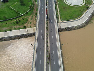 Aerial photograph showing a highway bridge spanning a wide river, surrounded by lush green...