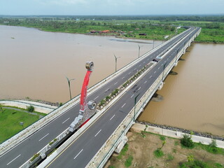Aerial photograph showing a highway bridge spanning a wide river, surrounded by lush green...