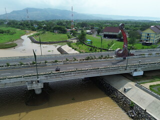 Aerial photograph showing a highway bridge spanning a wide river, surrounded by lush green...
