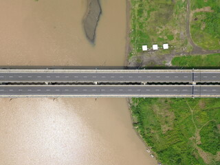 Aerial photograph showing a highway bridge spanning a wide river, surrounded by lush green...